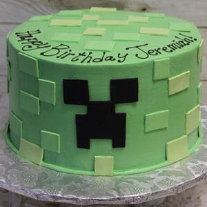 CB-011G is a round green cake featuring square fondant accents and a black Minecraft Creeper face, with "Happy Birthday Jeremiah!" written in black icing on the top edge.