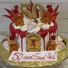 The BD-024F Fireball is a white cake with red drip icing, topped with mini Fireball whisky bottles, red and gold decorations, a gold 50 topper, and a "50 and Fired Up!" sign in front.