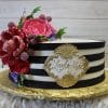 The BR-022 is a round cake with black and white stripes, topped with large red and pink sugar flowers, purple berries, green leaves, and a gold "Layla-Marie" plaque on the side. It sits on a gold board.