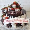 A chocolate-dripped cake (BD-065) topped with chocolate-covered strawberries features the name Naomi in white and red letters. A white plaque reads "Happy Birthday Naomi" in red script.
