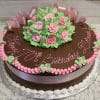 The AN-010 is a round chocolate cake with pink and green icing roses, a pink ribbon and border, "Happy 70th Birthday Doris!" written in pink icing, and presented on a silver tray.