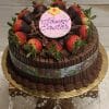 A chocolate cake with chocolate mousse filling, topped with a "Happy Easter" plaque, chocolate-dipped strawberries, and shavings, set on a gold cake stand with crystal accents.