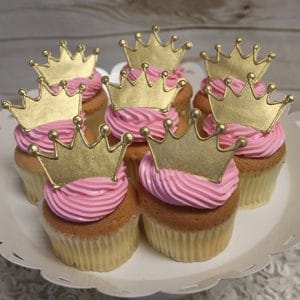 Gold cupcakes with chocolate filling, each topped with a gold crown decoration, arranged on a white cake stand.
