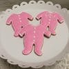 Three CE-004g baby shower cookies, shaped like pink onesies and decorated with white icing, are displayed on a scalloped white plate.
