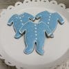 Three CE-004f baby shower cookies shaped like onesies, with blue icing, white polka dots, and collar details, arranged on a white scalloped-edge plate.