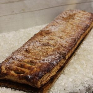 A rectangular puff pastry dusted with powdered sugar sits on a cardboard base, placed on a textured white surface.