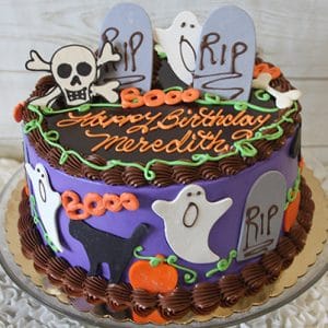 The HW-002 is a round purple and brown birthday cake topped with tombstones, ghosts, skulls, pumpkins, and “Happy Birthday Meredith” in orange icing; some decorations feature “RIP.”.