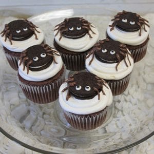 Six CC-058 Spider cupcakes—chocolate with white mousse filling—are topped with spider decorations and arranged on a glass plate.