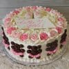The BB-013 is a round cake with pink and white icing roses, chocolate paw prints, frosting baby shoes on top, and a sign that says “It’s a Girl!” in pink script.