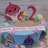 The CB-009A is a blue birthday cake featuring Baby Shark characters, colorful seashells, sand-like crumbs, a pink number 2, and a “Happy Birthday Azrielle!” sign on top.