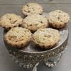 Six Mini Apple Tarts with crumb topping are displayed on an ornate silver cake stand with crystal details, set against a light wooden background.