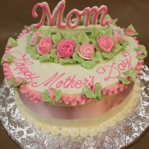 The MD-018 is a round cake with pink and green icing roses, green leaves, and "Mom" on top. "Happy Mothers Day" is written in pink icing. The cake comes on a decorative silver board.