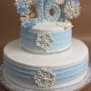 The TC-144 is a two-tiered white and light blue cake with white and blue snowflake designs, a silver-accented “16” topper, and sits on a foil-covered board—perfect for sweet sixteen celebrations.