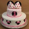 Two-tiered birthday cake (TC-142) decorated with Minnie Mouse ears and pink bows. The top tier is pink and white with a large bow and black ears; the bottom tier is white with Minnie Mouse silhouettes and pink bows.