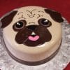 The CB-012B is a round cake designed as a cartoon pug face, featuring brown icing ears, big eyes, and a pink tongue on a silver floral-patterned board over red cloth.