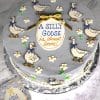 Gray cake decorated with cartoon geese, small flowers, and a message reading “A Silly Goose is almost done”